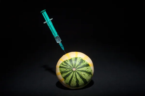 Genetically and chemically modified fruits and vegetables. Syringe stuck in a fruit. GMO food.