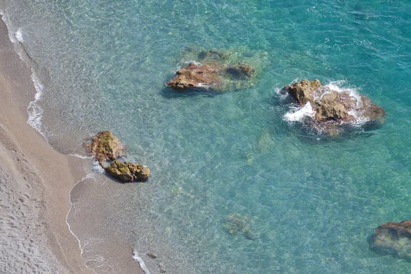Top view of a beach with golden sand, rocks and clear blue water