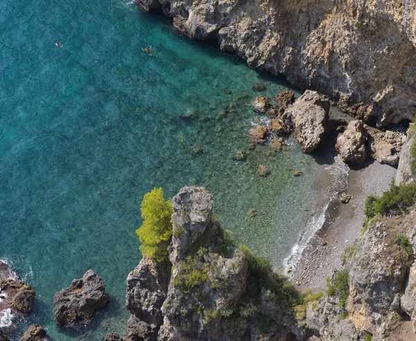 Top view of a beach with golden sand, rocks and clear blue water