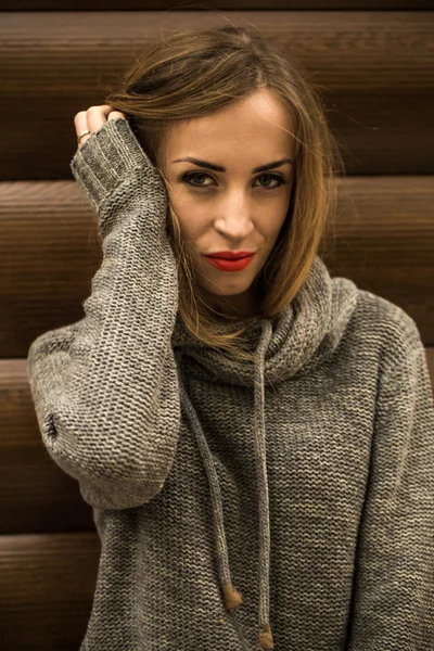 Beautiful girl in a sweater with long hair and red lips on the background of wooden logs