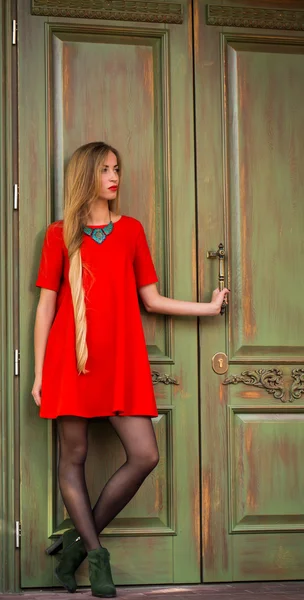Fashionable young girl on a background of vintage door in  red dress with long hair