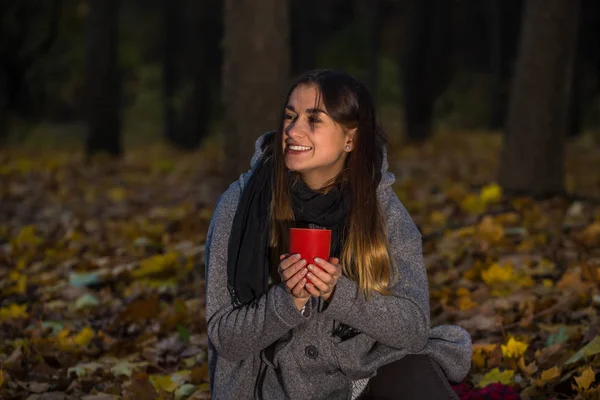Beautiful girl in autumn forest with a hot Cup of tea