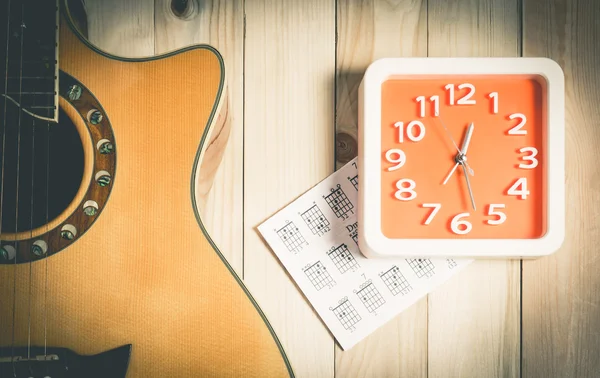 Music Practice time concept with acoustic guitar and orange wall clock