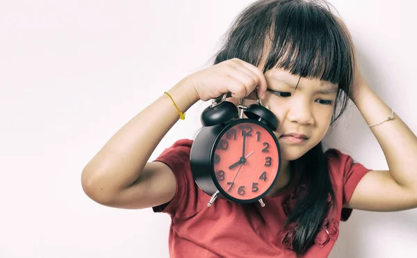 Little asian girl is angry at the alarm clock for waking her up. A kid in red shirt is upset that the alarm clock wake up her so early. Lazy Japanese girl doesn\'t want to get up in the morning.