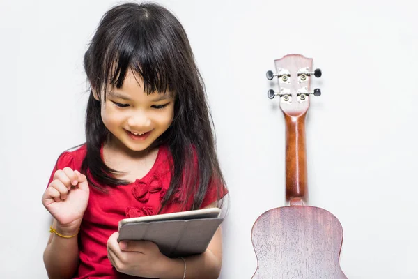 Asian girl is using her tablet to learn to play music. Japanese girl having fun learning guitar on her music application tablet. Little girl enjoying virtual music playing on tablet than real guitar.