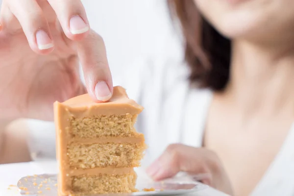 Cute Asian girl is using her hand to eat that piece of cake. Japanese girl is eating cake on white background. Chinese girl is eating orange cake using her hand.