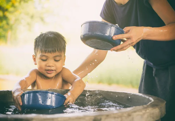 Mother is taking a bath for her son in country water well.