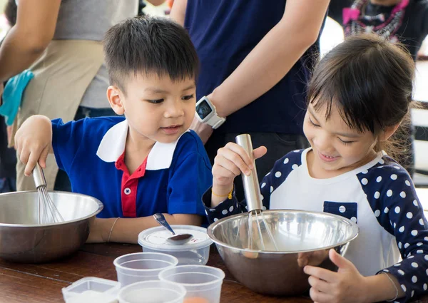 Asian children enjoying educational cooking class. They making homemade ice cream with family. Homemade baking and cooking with family help child develop skills. Children learning to use baking tool.