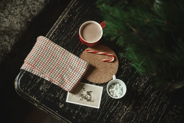 Cocoa in a red cup near, postcards under the checkered towel, lollipop on a stand of cork, cup with marshmallow