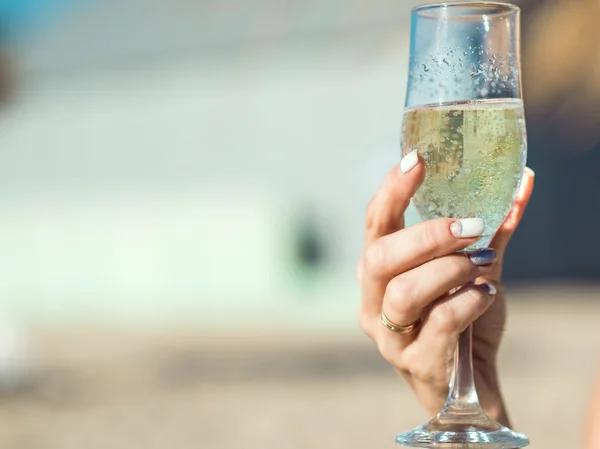 Female hand with delicious manicure holding a glass of sparkling wine on the sun. Vague background.