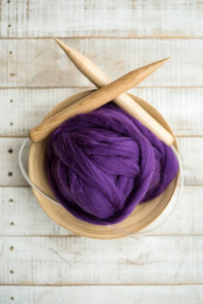 Wooden knitting needles and purple merino wool ball in a basket