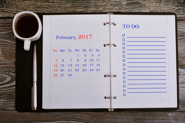 February 2017 - Calendar. To do list is written on notepad with metal pen on wooden background, business concept