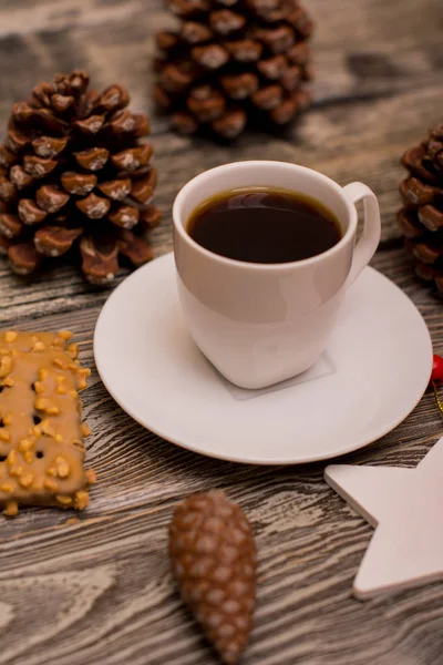 Small white cup of coffee, cocoa beans, hazelnuts, cookies, cone, christmas decoration on wooden background