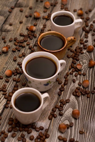 Four cups of coffee, hazelnuts and cocoa beans on wooden background