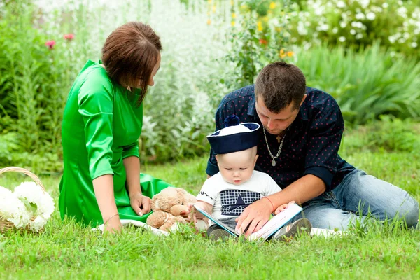 Young family reads reads son a story in the Park on the grass