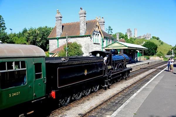 LSWR T9 Class 4-4-0 steam train entering the railway station with the castle to the rear, Corfe.