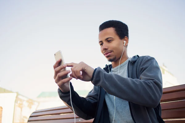 Man in sports uniform and headphones is listening to music using a smartphone