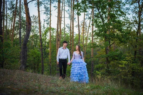 A love story couple, in love, together in the forrest park, girl in a beautiful violet dress,  evening, summer, holding each other, near the pine tree