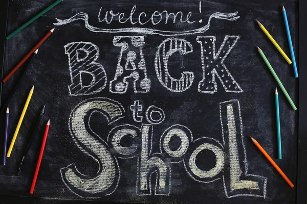 Back to school background with laid out flat different color pencils on black chalkboard texture. Top view.