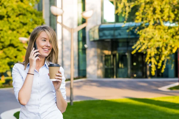 Business, technology and people concept - smiling businesswoman with smartphone over office building