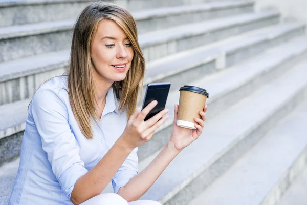 Young smart professional woman reading using phone. Female businesswoman reading news or texting sms on smartphone while drinking coffee on break from work