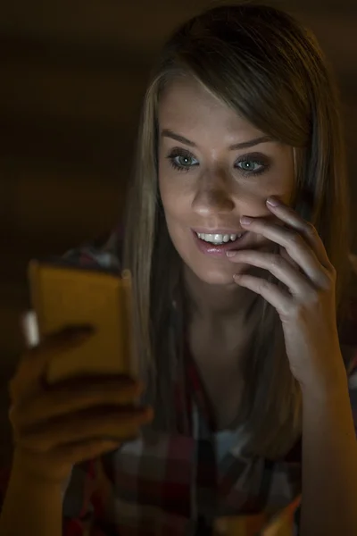 Gorgeous young woman standing with mobile phone at night street outdoors, female caucasian student reading text messages on her cell phone with reflected on her face screen light, blank screen phone