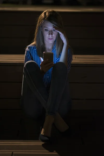 Closeup side view portrait of young sad thoughtful woman leaning against street lamp at night on bokeh copy space background, Upset young woman with mobile phone reads the message.