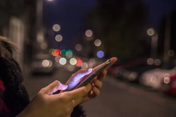 Female hand holding touch screen mobile phone on blurred night lights background