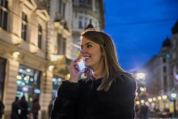 Portrait of a beautiful girl. gorgeous brunette girl, portrait in night city lights. Beautiful girl texting with smart phone. Young businesswoman having a conversation using a smartphone on a phone call