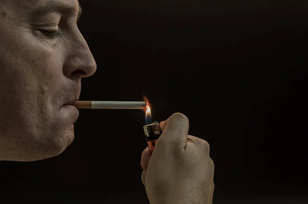 Man smoking cigarette on black background. Mystery man with cigar and smoke isolated on black background. dark and sullen shot of a young man smoking over a black background