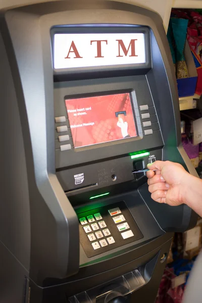 Young man using ATM cash machine in the store or gas station, to pay for his bill