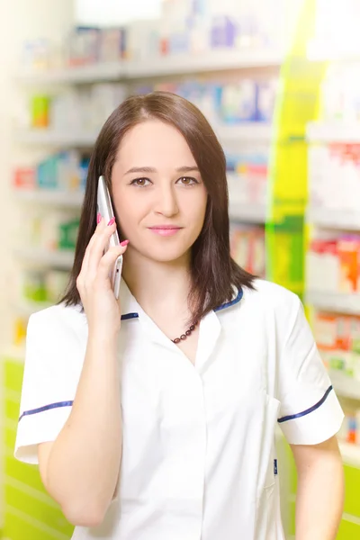 Young pharmacist woman expressing wonder while having a phone call. Pharmaceutical background. Drugstore. Pills and medicine.