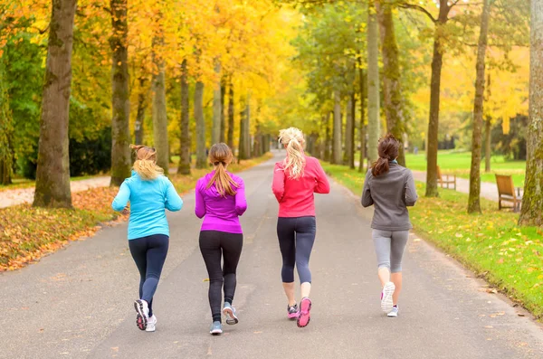 Four female friends running together in autumn