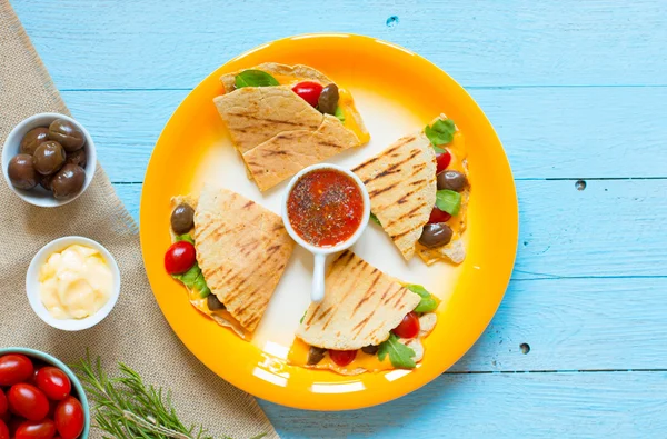 Delicious veggie quesadillas with tomatoes, olives, and cheddar cheese in a colorful dish over a wooden