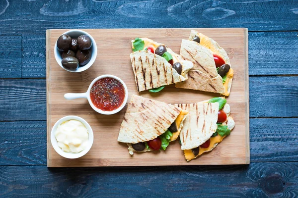 Delicious veggie quesadillas with tomatoes, olives, and cheddar cheese in a colorful dish over a wooden