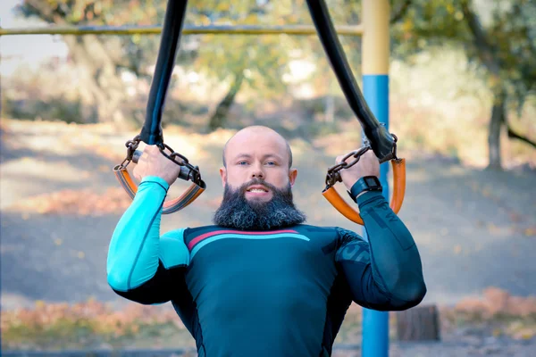 Muscular bearded man training with straps