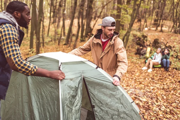 Men pitching tent in autumn forest