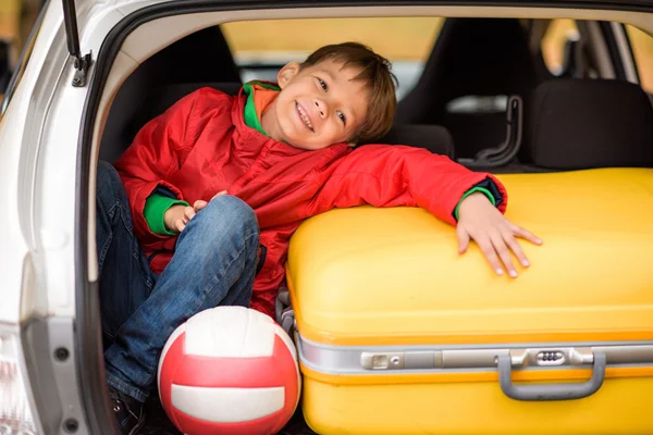 Smiling boy sitting in car trunk