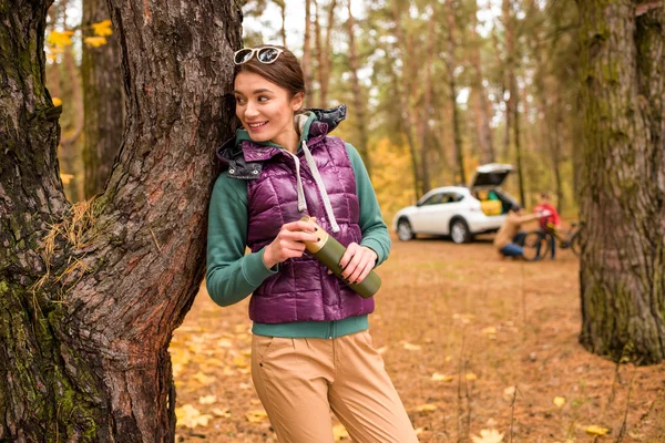 Smiling woman with thermos in autumn forest