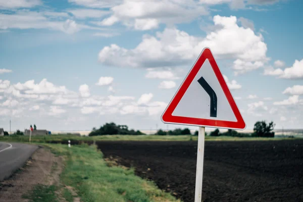 Traffic sign on a blurred background with clouds, field, road