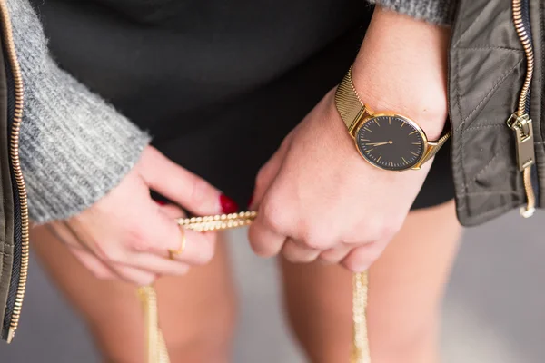 Fashion details, young business woman holding her bag. wearing golden jewelry, and watch. graded in warm colors.
