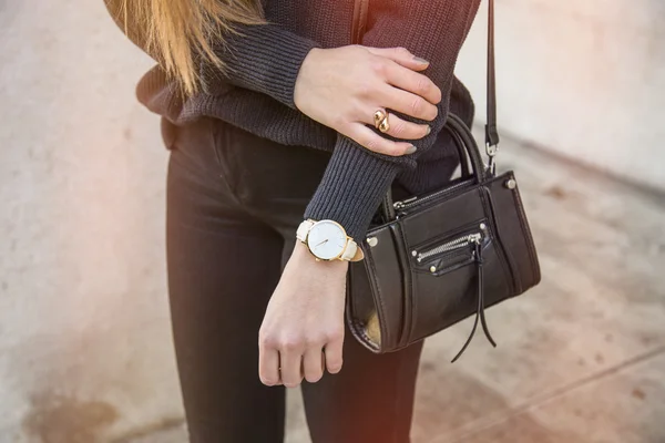 Fashion details, young business woman holding her bag. wearing golden jewelry, and watch.