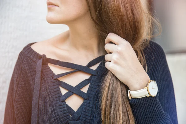 Fashion details, young stylish woman wearing a golden watch and a lace up oversized navy blue sweater. graded in warm colors.