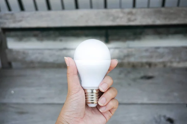 Bright LED bulb in hand with wooden bench background