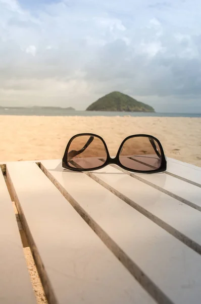 Black Sun glasses on white wooden table  with the beach background  and sunny light in the morning