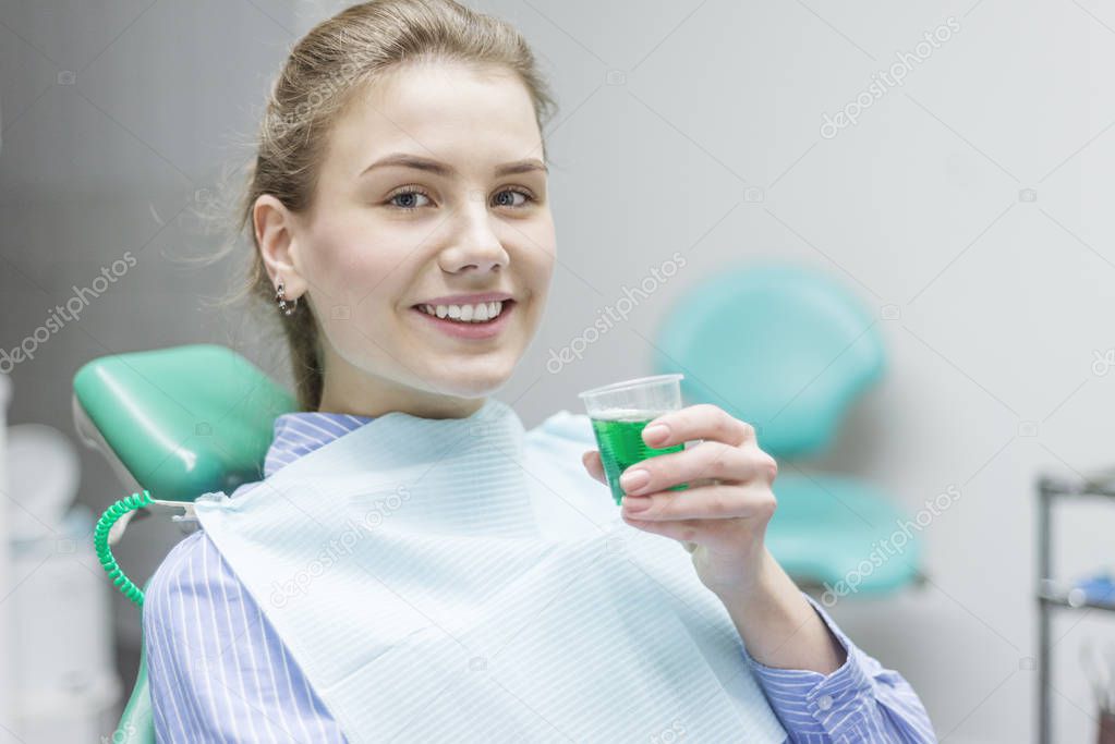 female patient rinsing mouth with dentist in background at clini