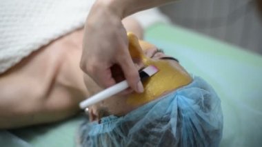 Yüz, kozmetik tedavi spa adlı sahip kadın altın yüz maskesi uygulamak güzellik uzmanı. Erkek güzellik salonunda üzerinde profesyonel güzellik uzmanı. Cilt prosedürler kozmetik temizlik.