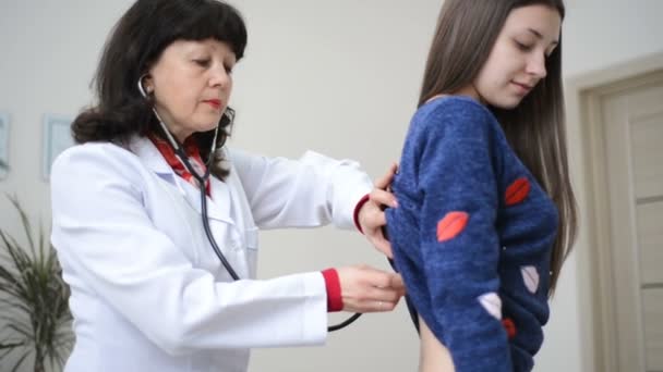 Ο γιατρός τον έλεγχο ή την εξέταση ausculting πνεύμονες στο πίσω μέρος νέοι Θηλυκός ασθενής με στηθοσκόπιο — Αρχείο Βίντεο