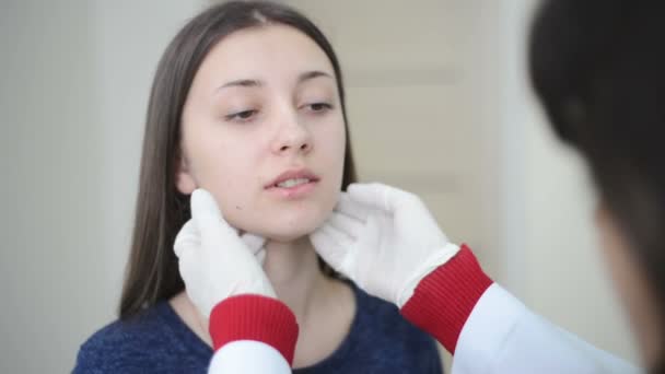 Врач проверяет или проверяет горло или шею молодой пациентки — стоковое видео