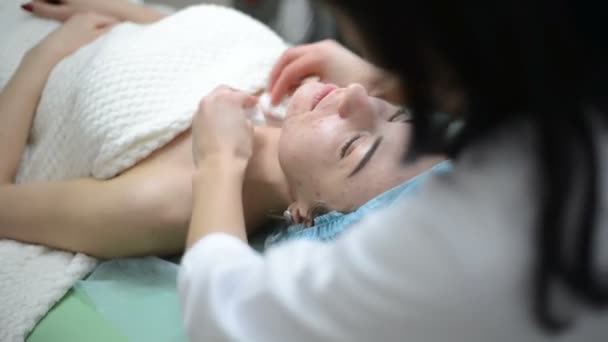 Cosmetologist κρέμα γάλακτος για το προσώπου και μασάζ γυναίκα έχοντας καλλυντικά θεραπεία στο spa. Επαγγελματίας αισθητικός εφαρμογή μάσκας σε γυναίκα στο σαλόνι ομορφιάς. Facial διαδικασίες δέρμα καθαρισμού κοσμετολογία. — Αρχείο Βίντεο